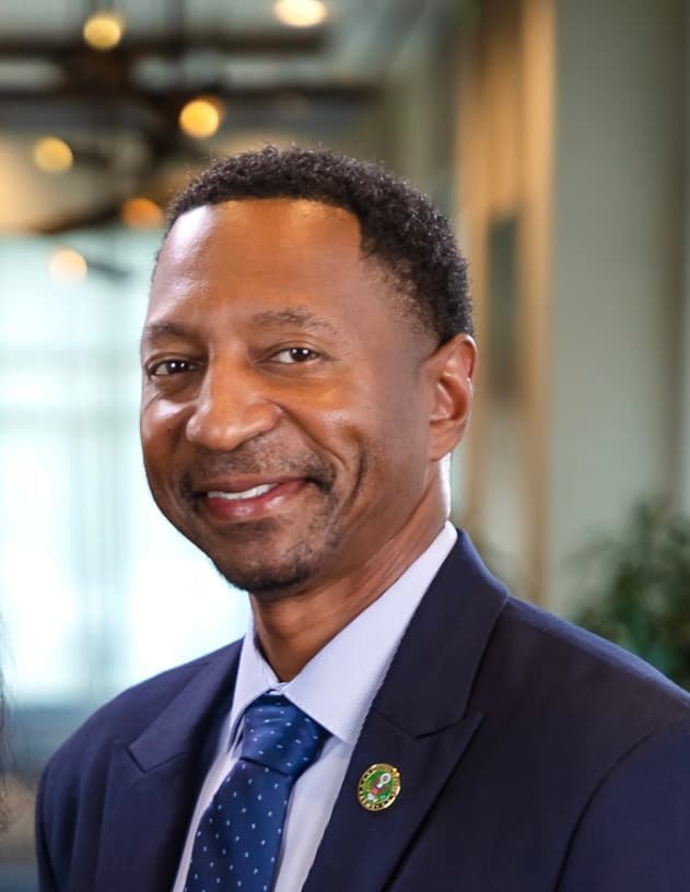 Smiling Black man in a navy suit and blue patterned tie against a blurred background.